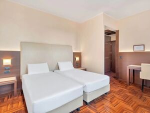 Two twin beds with white linens and headboard in a beige room with wooden floor at B&B Hotel Habitat Giussano