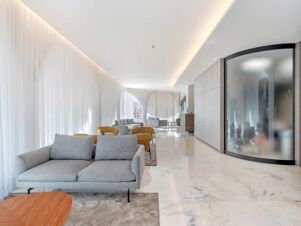Spacious lobby area of B&B Hotel Habitat Giussano with grey sofas, mustard chairs, marble floor, and large frosted glass window
