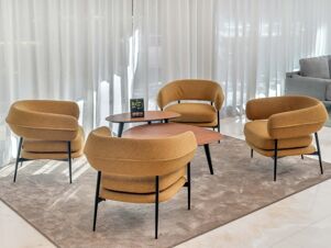Four mustard yellow chairs with black legs around two wooden tables on a gray rug in B&B Hotel Habitat Giussano