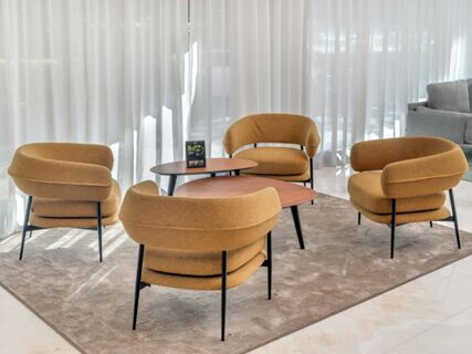 Four mustard yellow chairs with black legs around two wooden tables on a gray rug in B&B Hotel Habitat Giussano