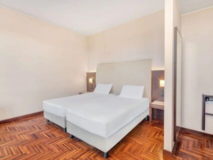 Two single beds with white linens and pillows in a room with wooden floors and beige walls at B&B Hotel Habitat Giussano