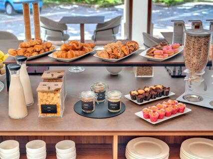 Croissants, donuts, muffins, cereals, milk, nuts, and plates neatly arranged on a breakfast buffet at B&B Hotel Habitat Giussano