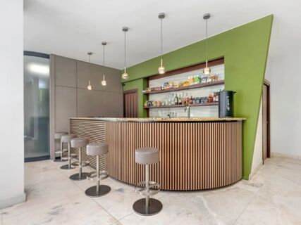 Modern bar area with five round stools, hanging pendant lights, and shelves with drinks at B&B Hotel Habitat Giussano