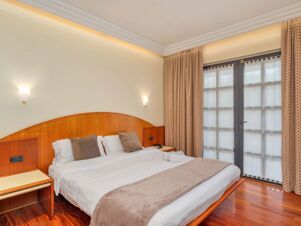 Double bed with headboard, beige pillows, bedside tables, wall lights, curtains, and door in B&B Hotel Hotel Prestige Ornago