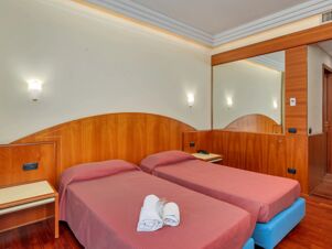 Two single beds with red striped bedspreads and rolled white towels in a room at B&B Hotel Hotel Prestige Ornago