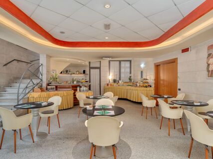 Dining area with round tables, white and brown chairs, buffet tables with yellow cloths, and stairs at B&B Hotel Hotel Prestige Ornago