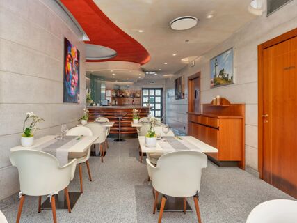 Dining area with white tables and chairs, a bar, colorful wall art, and modern ceiling design at B&B Hotel Hotel Prestige Ornago
