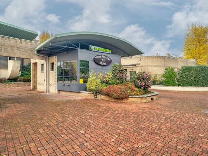 Modern building entrance with green curved canopy, plants, and signage for B&B Hotel Hotel Prestige Ornago surrounded by trees