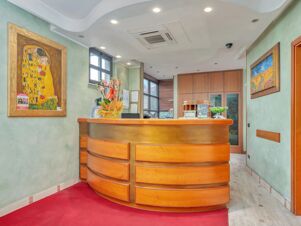 Reception area with wooden desk, two paintings, orchid flower, and green walls at B&B Hotel Hotel Prestige Ornago