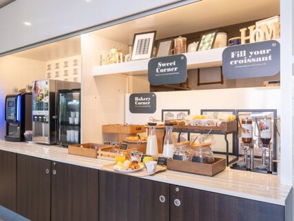 Self-service breakfast area with coffee machines, cereal jars, pastries, milk pitchers, and signs at B&B Hotel Mantova