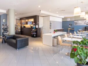Reception area with black leather couches, a snack display, white tables with beige chairs, and B&B Hotel Mantova sign