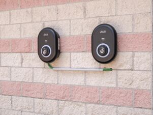 Two black electric vehicle charging stations mounted on a brick wall with pink and beige stones at B&B Hotel Mantova