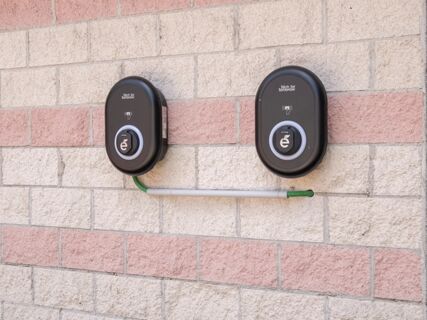 Two black electric vehicle charging stations mounted on a brick wall with pink and beige stones at B&B Hotel Mantova