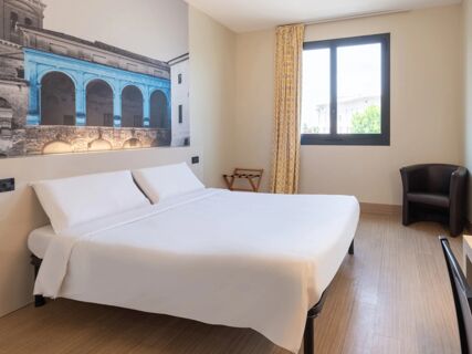 Double bed with white linens below a large mural next to a window with yellow patterned curtains at B&B Hotel Mantova