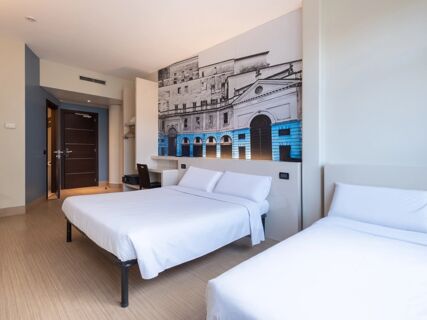 Two beds with white linens, a wooden chair, desk, and large black and white architectural print in a room at B&B Hotel Mantova
