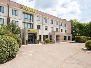 Exterior view of the multi-story B&B Hotel Mantova building with large windows and green bushes along the driveway