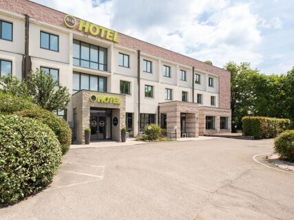 Exterior view of the multi-story B&B Hotel Mantova building with large windows and green bushes along the driveway
