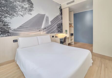 Minimalist hotel room at B&B Hotel Milano Cenisio Garibaldi featuring a large bed with white bedding and a black and white cityscape mural