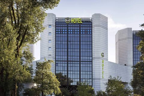 Modern high-rise building with large glass windows and white stone walls surrounded by trees at B&B Hotel Milano Cenisio Garibaldi