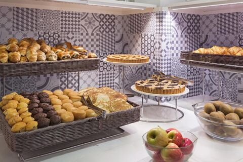 Various bakery items including muffins, croissants, pancakes, pies, and bowls of apples and kiwis at B&B Hotel Milano Cenisio Garibaldi