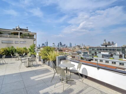 Outdoor terrace with metal chairs and tables surrounded by plants overlooking the cityscape from B&B Hotel Milano City Center Duomo
