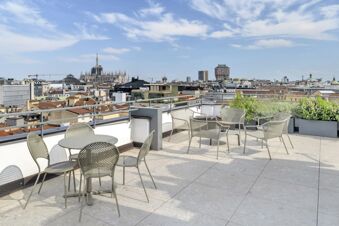 Outdoor rooftop terrace with tables, chairs, plants, and a view of the Milan skyline including the Duomo from B&B Hotel Milano City Center Duomo
