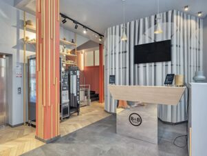 Reception area of B&B Hotel Milano City Center Duomo with curved gray wall, wooden front desk, vending machines, and pendant lights