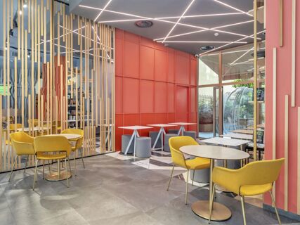 Bright seating area with yellow chairs, pink partition, geometric ceiling lights, and marble flooring at B&B Hotel Milano City Center Duomo