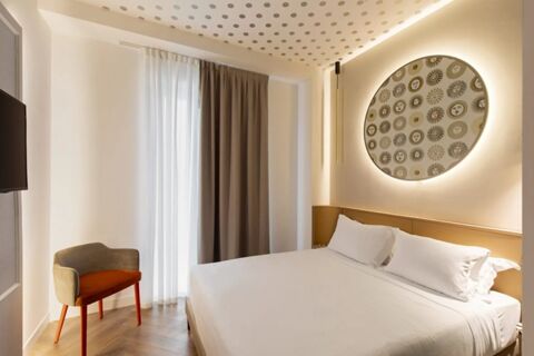 Minimalist bedroom interior at B&B Hotel Milano Duomo Velasca with a large bed, patterned wall art, and a small armchair near curtains