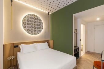 Modern hotel room at B&B Hotel Milano Duomo Velasca with white bed, green and beige walls, decorative round wall art, and wood floor