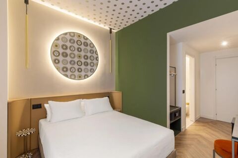Modern hotel room at B&B Hotel Milano Duomo Velasca with white bed, green and beige walls, decorative round wall art, and wood floor