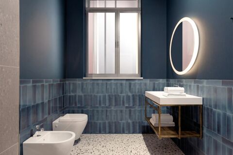 Bathroom interior at B&B Hotel Milano Duomo Velasca with blue tiled walls, white bidet and toilet, window, and illuminated round mirror