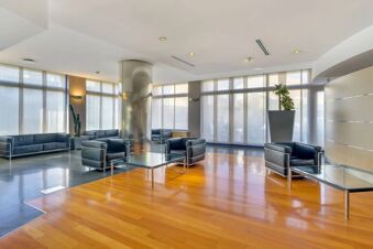 Modern hotel lobby with black leather sofas and armchairs around glass coffee tables near large windows at B&B Hotel Milano La Spezia
