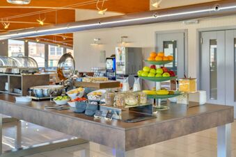 Buffet area with fresh fruit, cereals, bread rolls, vegetables, and milk bottles in the breakfast room at B&B Hotel Milano La Spezia