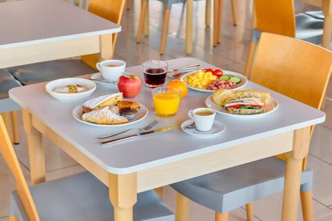 Breakfast spread on a table with croissants, yogurt, fruits, juice, coffee, and scrambled eggs at B&B Hotel Milano La Spezia