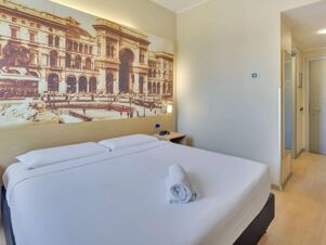 Double bed with white linens and rolled towel inside a room featuring a large mural and mirror at B&B Hotel Milano La Spezia