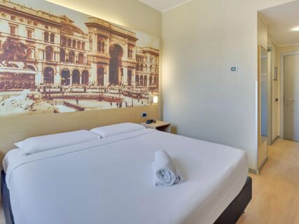 Double bed with white linens and rolled towel inside a room featuring a large mural and mirror at B&B Hotel Milano La Spezia