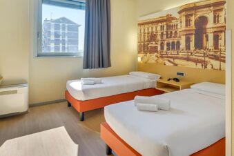 Two single beds with white linens and towels in a room with a large wall art and window at B&B Hotel Milano La Spezia
