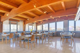 Dining area with tables and chairs under wooden ceiling beams featuring bird-shaped lights at B&B Hotel Milano La Spezia