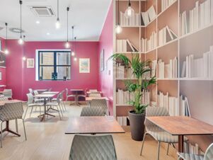 Dining area at B&B Hotel Milano San Siro with pink walls, white chairs, wooden tables, hanging light bulbs, and a plant