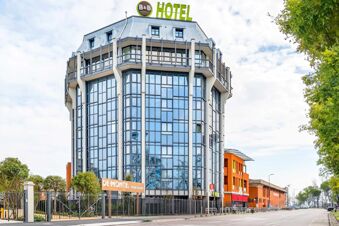 Modern multi-story building with large glass windows and balconies topped by green "HOTEL" signage for B&B Hotel Milano San Siro