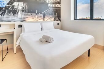 White bed with folded towels on top next to a window and black and white wall art in B&B Hotel Milano San Siro