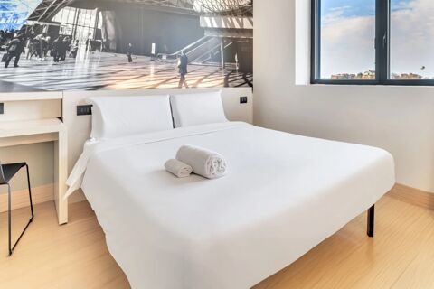 White bed with folded towels on top next to a window and black and white wall art in B&B Hotel Milano San Siro