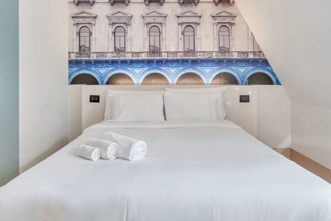 White bed with pillows and rolled towels in front of a wall mural showing building arches at B&B Hotel Milano San Siro
