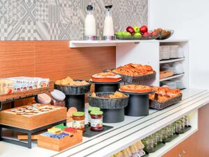 Breakfast buffet with assorted pastries, fresh fruit, milk carafes, preserves, and tea packets at B&B Hotel Milano San Siro