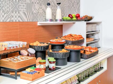 Breakfast buffet with assorted pastries, fresh fruit, milk carafes, preserves, and tea packets at B&B Hotel Milano San Siro