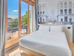 Double bed with white linens next to a large window leading to a balcony at B&B Hotel Milano Sant'Ambrogio