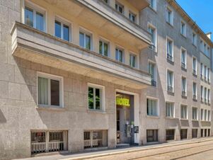 Exterior view of the stone facade of B&B Hotel Milano Sant'Ambrogio showing multiple windows and the hotel entrance with a green sign