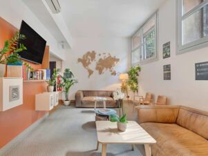 Reception area of B&B Hotel Milano Sant'Ambrogio with leather sofas, potted plants, wall-mounted TV, and wooden world map decor