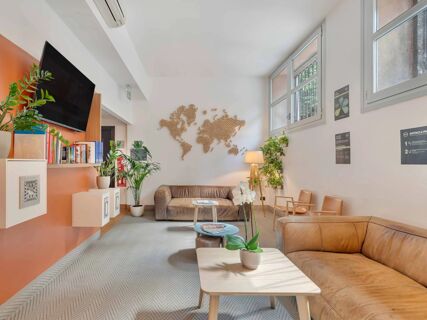 Reception area of B&B Hotel Milano Sant'Ambrogio with leather sofas, potted plants, wall-mounted TV, and wooden world map decor
